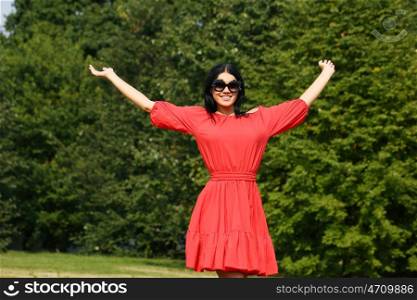 Beautiful young woman in red dress walking in summer park