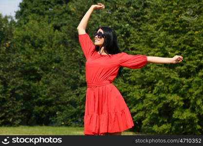 Beautiful young woman in red dress walking in summer park