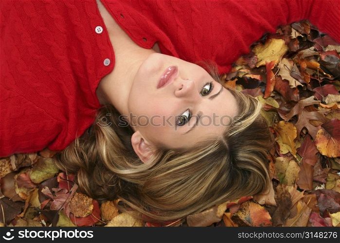 Beautiful young woman in red sweater laying in a bed of fall colored leaves.