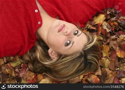 Beautiful young woman in red sweater laying in a bed of fall colored leaves.