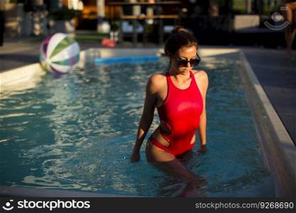 Beautiful young woman in red swimwear relaxing by the  swimming pool