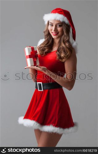 Beautiful young woman in Santa dress and hat celebrating Christmas holding gift box. Woman in santa dress with gift