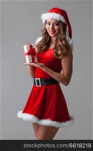 Beautiful young woman in Santa dress and hat celebrating Christmas holding gift box. Woman in santa dress with gift