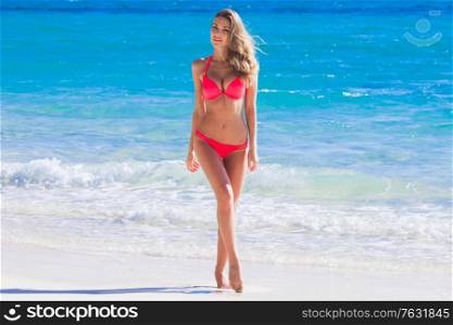 Beautiful young woman in sexy bikini standing at tropical sea beach. Young woman in red bikini