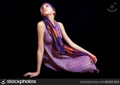 Beautiful young woman in sundress sitting on a black background