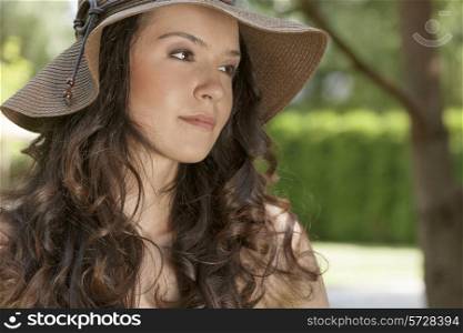 Beautiful young woman in sunhat looking away in park