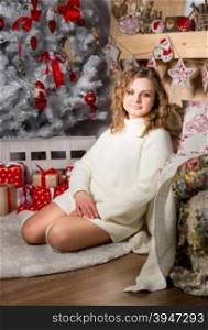 Beautiful young woman in sweater sitting on floor under Christmas tree