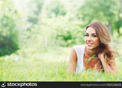 Beautiful young woman in white dress lying on grass. Young woman in white dress on grass