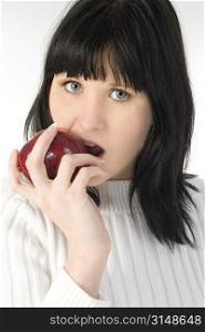 Beautiful young woman in white sweater eating red apple.