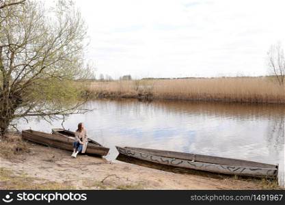 beautiful young woman is sitting and having fun in a boat near the river in spring day. beautiful young woman is sitting and having fun in a boat near the river in spring day.