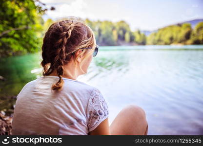 Beautiful young woman is sitting by a lake and enjoying the day