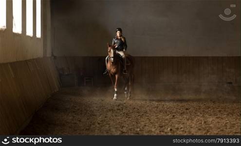 Beautiful young woman jockey doing training at riding hall