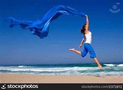 Beautiful young woman jumping on the beach with a colored tissue