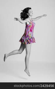 Beautiful young woman jumping, partially desaturated with only the dress with color