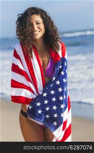 Beautiful young woman laughing wearing bikini and wrapped in American flag towel on a sunny beach