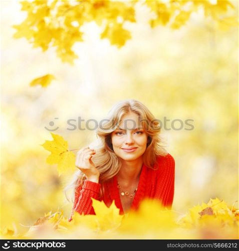 Beautiful young woman laying on yellow leaves in autumn park