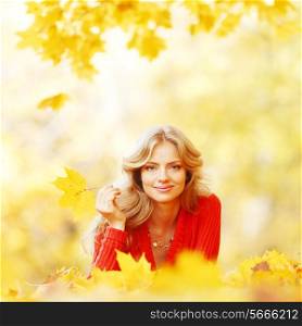 Beautiful young woman laying on yellow leaves in autumn park