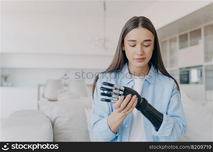 Beautiful young woman learns to install her bionic prosthetic arm, sitting on sofa at home. Modern girl with disability puts together artificial limb. High tech medical care of disabled people.. Beautiful young woman learns to install her high tech bionic prosthetic arm, sitting on sofa at home
