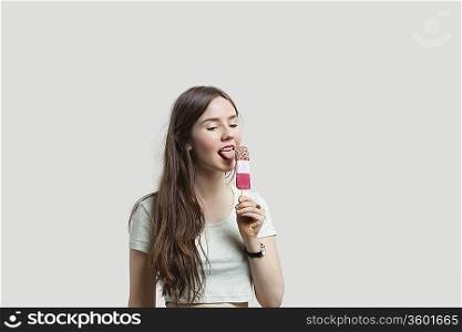 Beautiful young woman licking popsicle over gray background