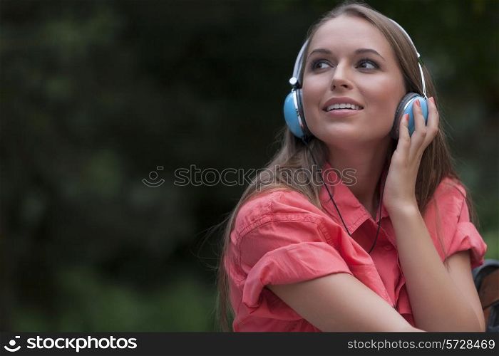 Beautiful young woman listening to headphones in park