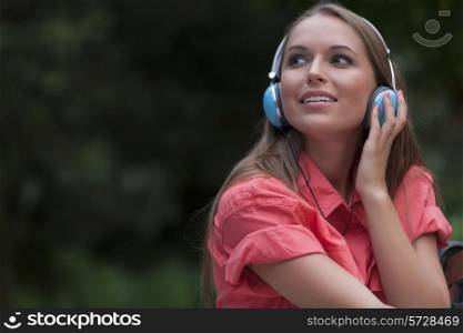 Beautiful young woman listening to headphones in park