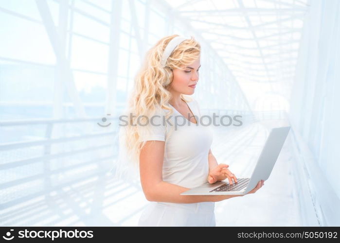 Beautiful young woman listening to the music in headphones, surfing internet via laptop and buying music online.