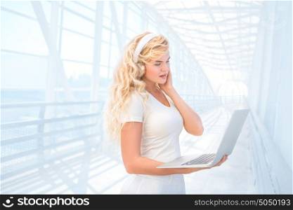Beautiful young woman listening to the music in headphones, surfing internet via laptop and buying music online.