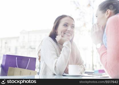 Beautiful young woman looking at friend sharing secrets at outdoor cafe