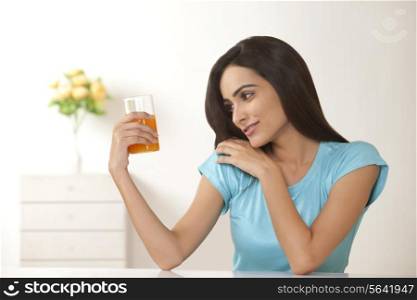Beautiful young woman looking at glass of orange juice at home