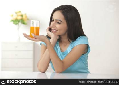 Beautiful young woman looking at glass of orange juice at home