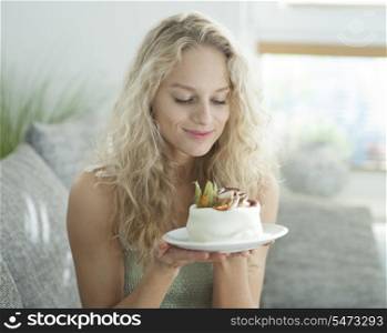 Beautiful young woman looking at tempting cake in house