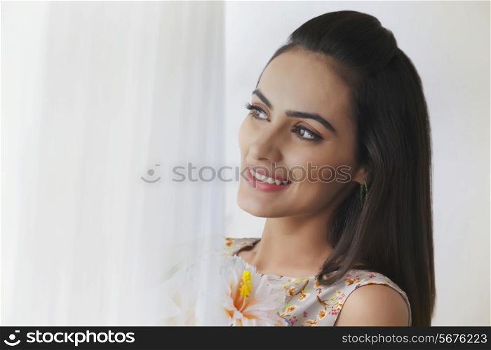 Beautiful young woman looking away by curtain