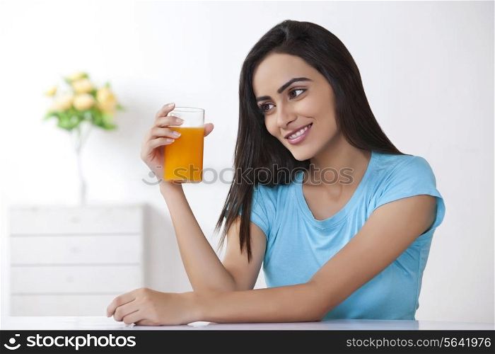 Beautiful young woman looking glass of orange juice at home