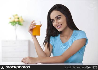 Beautiful young woman looking glass of orange juice at home