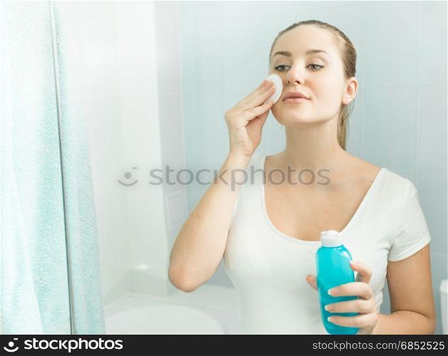 Beautiful young woman looking in the mirror and using cleaning lotion