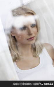 Beautiful young woman looking through hotel window