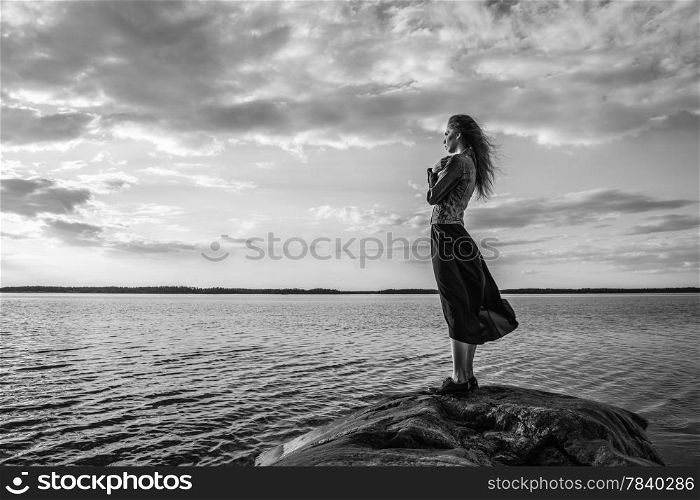 Beautiful young woman looks at the horizon on shore, wind blowing and cloudy sky - black and white image
