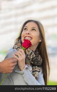 Beautiful young woman looks up while receiving a red rose on an out of focus background. Valentine?s concept.. Young woman looks up receiving a rose