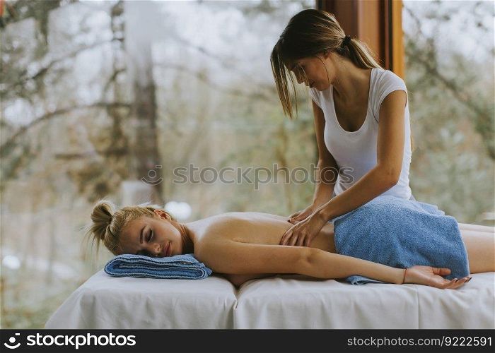 Beautiful young woman lying and having back massage in spa salon during winter season