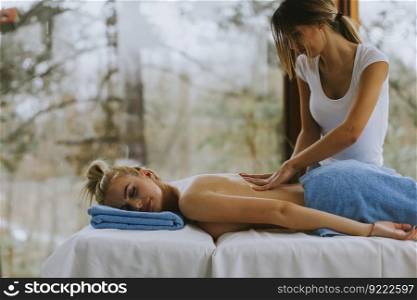 Beautiful young woman lying and having back massage in spa salon during winter season