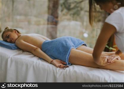 Beautiful young woman lying and having leg massage in spa salon during winter season