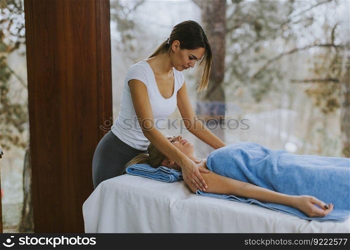 Beautiful young woman lying and having shoulder massage in spa salon during winter season