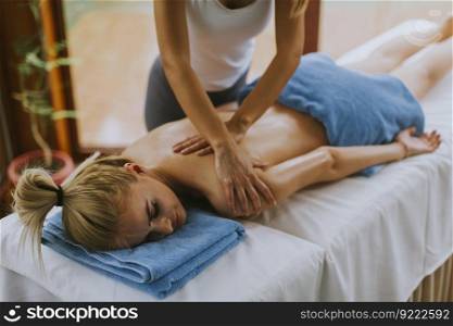 Beautiful young woman lying and having shoulder massage in spa salon during winter season