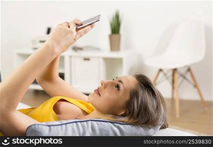 Beautiful young woman lying on a sofa and send text messages