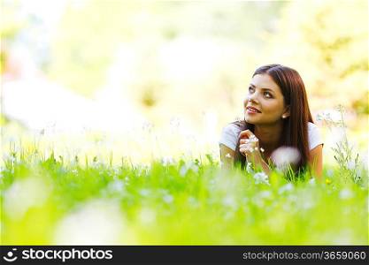 Beautiful young woman lying on grass with flowers