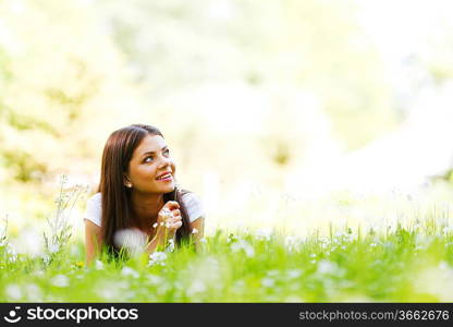 Beautiful young woman lying on grass with flowers