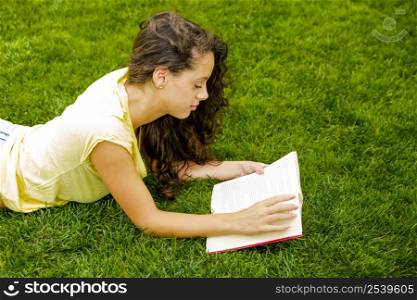 Beautiful young woman lying on the grass and reading a book