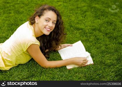 Beautiful young woman lying on the grass and reading a book