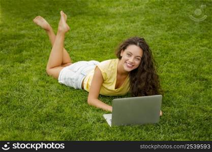 Beautiful young woman lying on the grass and working with a laptop
