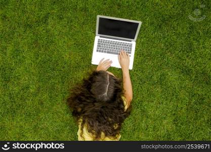 Beautiful young woman lying on the grass and working with a laptop